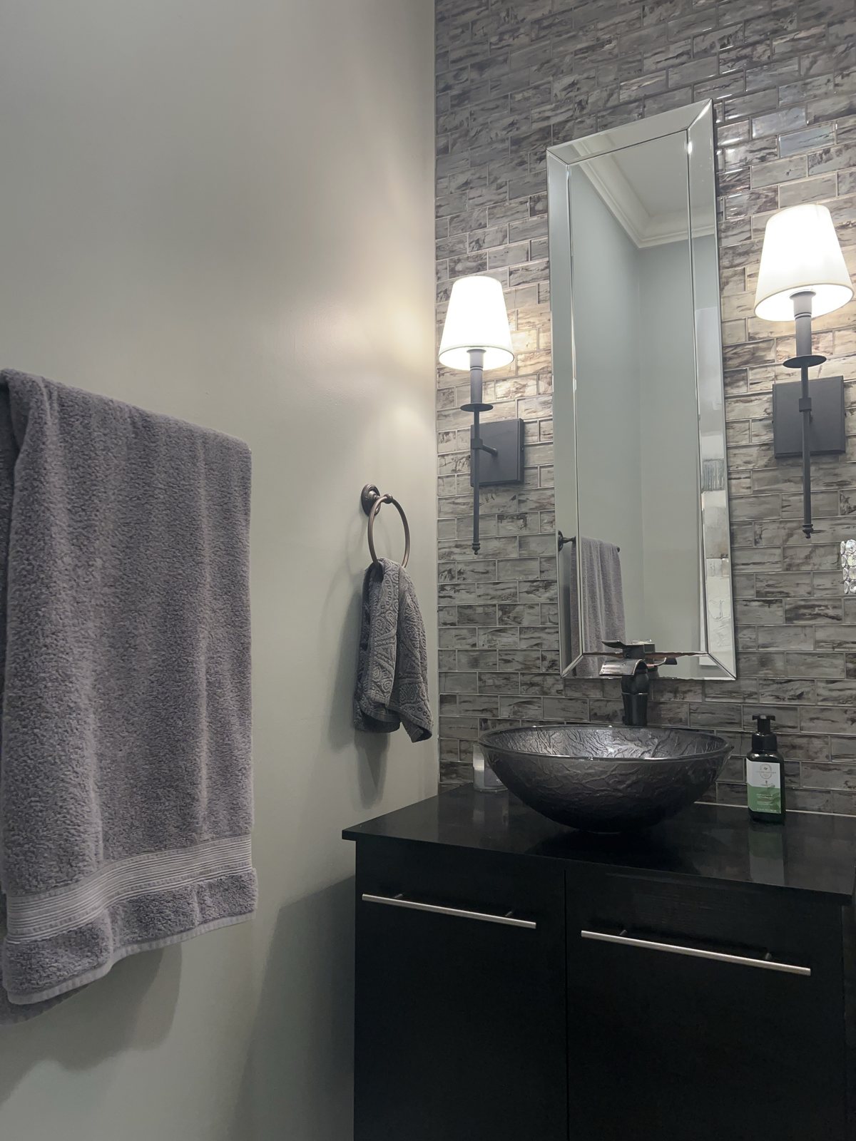 Finished bathroom vanity with glass tile accent wall, mirror, and wall sconces