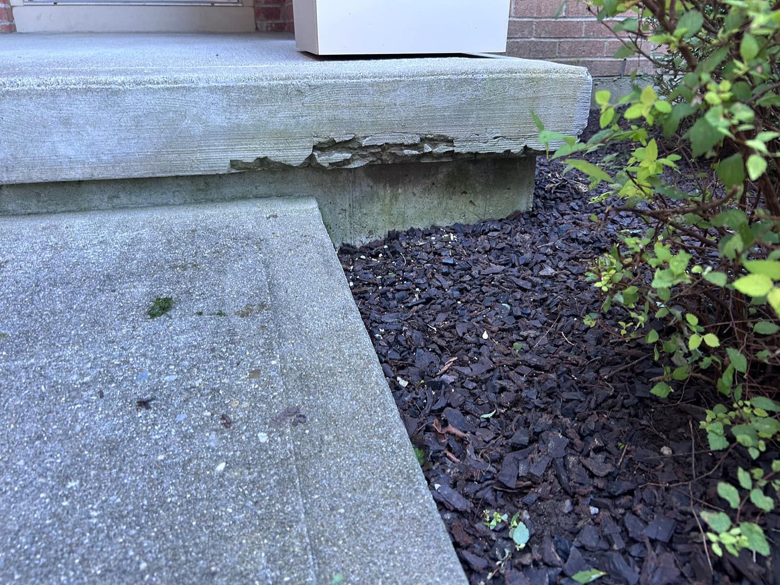 Spalled concrete along the front edge of a porch before repair