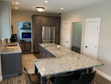 Finished kitchen with gray cabinetry, granite island, and adjoining dining seating