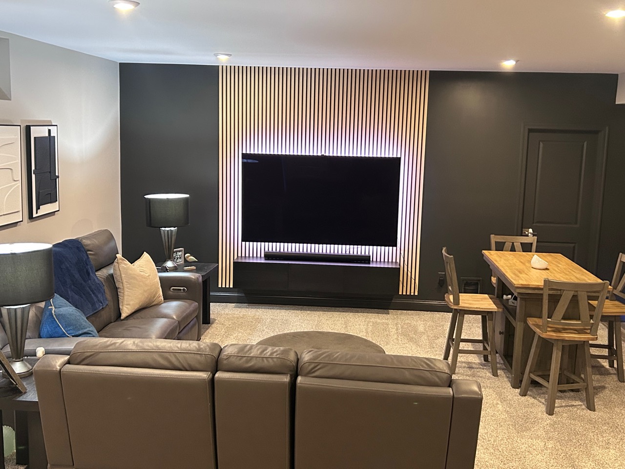 Finished TV feature wall with vertical wood slats, accent lighting, soundbar, floating console, and furnished seating area
